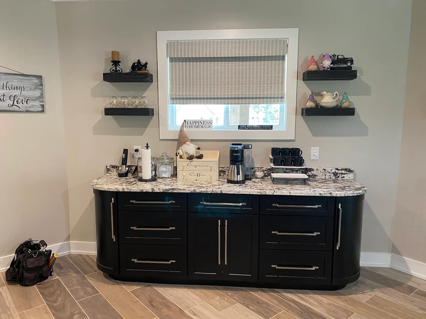 Black bathroom vanity with a stone countertop and floating shelves beside the window