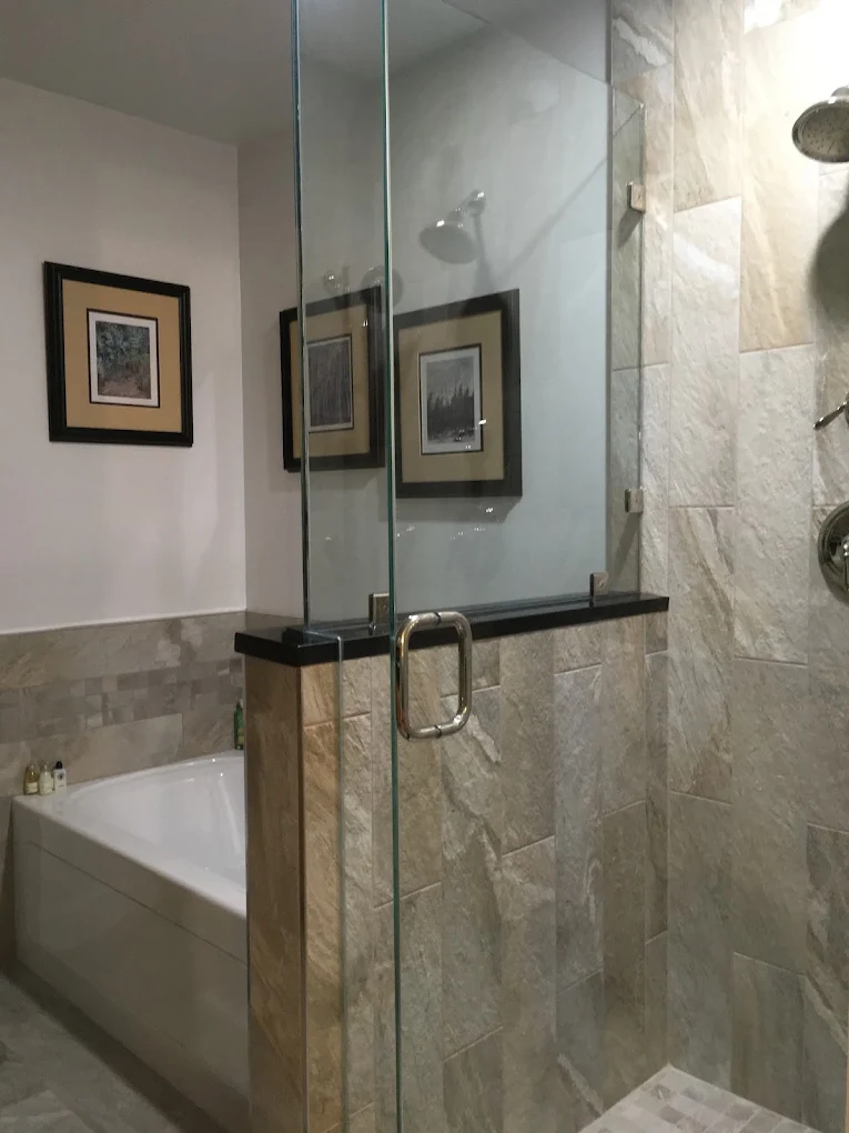Glass-enclosed shower with stone-look wall tiles beside a bathtub