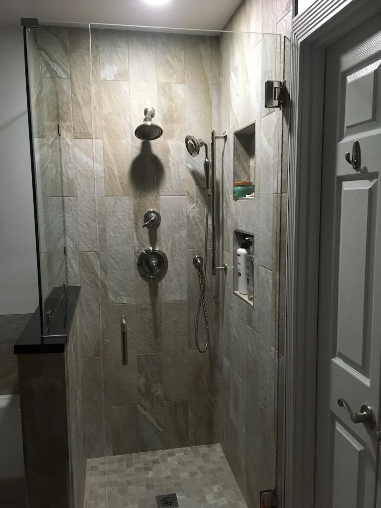 Glass-enclosed walk-in shower with stone-look tiles and dark fixtures