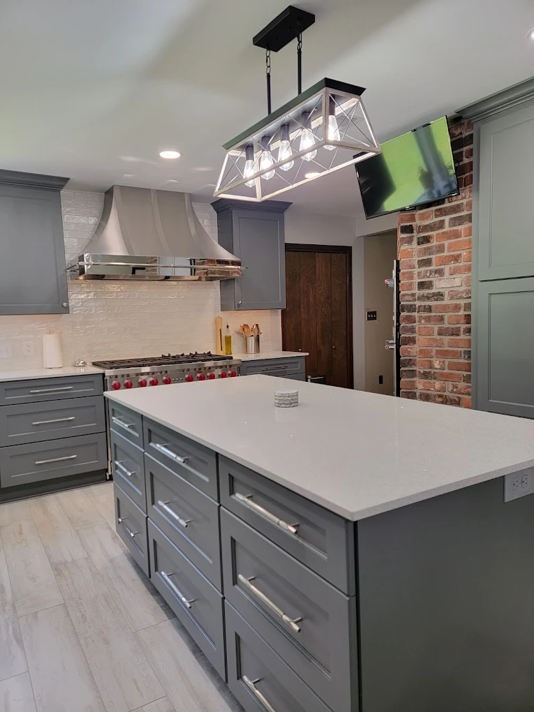 Kitchen with a gray island, white countertop, pendant lighting, and exposed brick wall