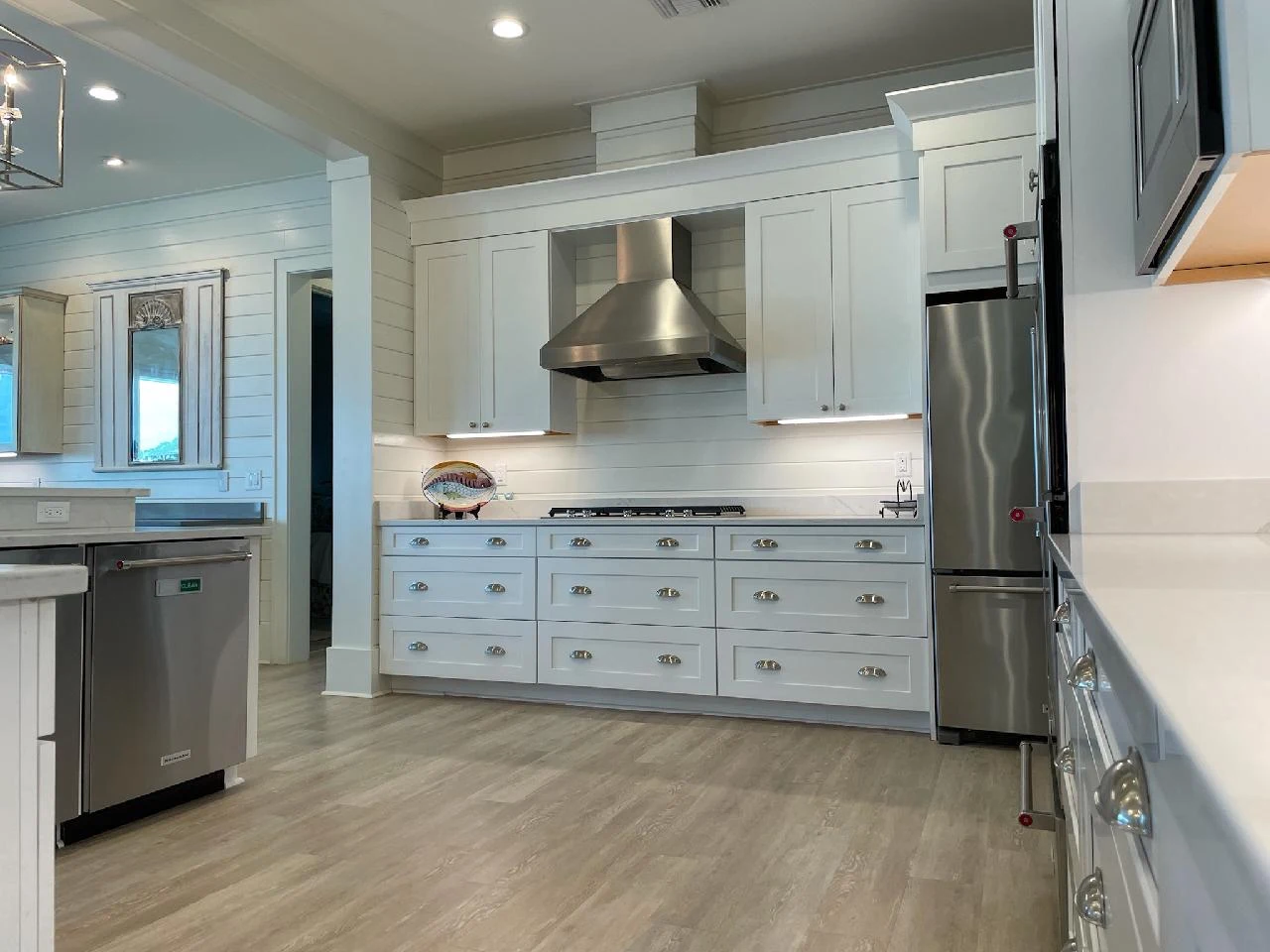 White kitchen cabinets with a stainless steel range hood and wood-look flooring