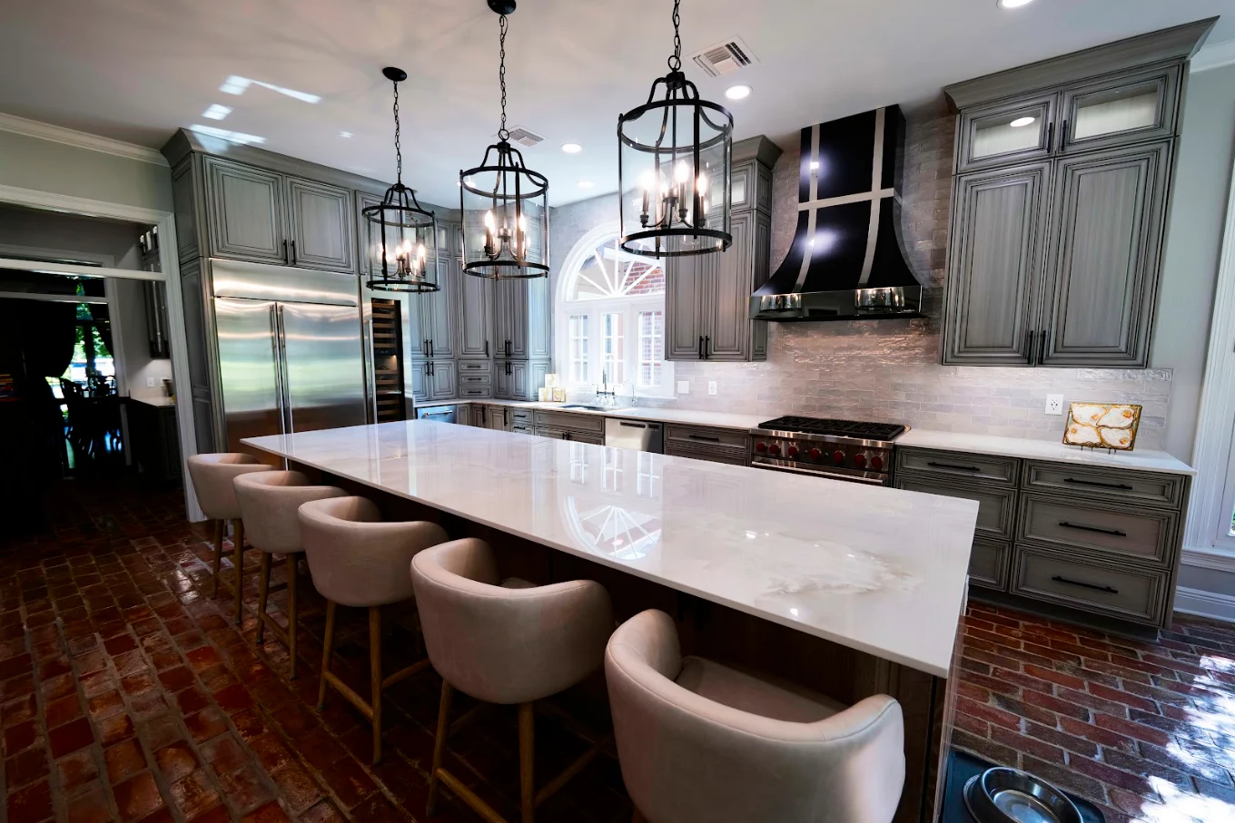 Kitchen with a large white island, upholstered bar stools, gray cabinets, and brick flooring